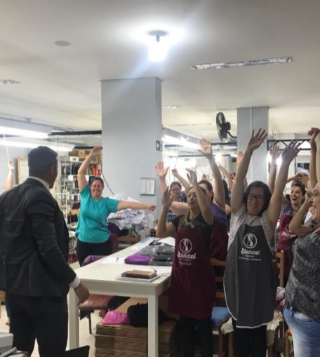 Funcionárias de uma fábrica de braços erguidos durante dinâmica do treinamento